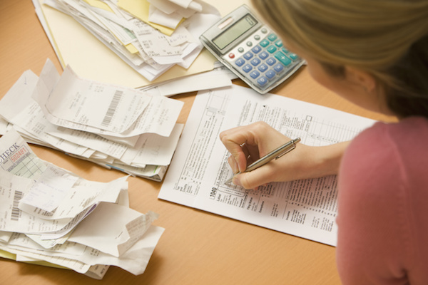 Young woman fills out tax information at her desk with piles of receipts.  Horizontal shot.