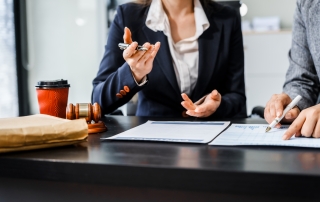 Two female lawyers in business suits meet at wooden desk, shaking hands over contract paper. wooden gavel and scales justice as discuss legal compliance, corporate law, dispute resolution.
