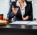 Two female lawyers in business suits meet at wooden desk, shaking hands over contract paper. wooden gavel and scales justice as discuss legal compliance, corporate law, dispute resolution.